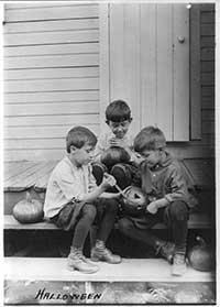 Three boys outside carving pumpkin.