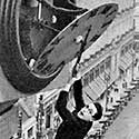 Man dangling from clock over city street.