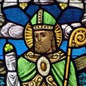 Saint Patrick dressed in green holding a shamrock.