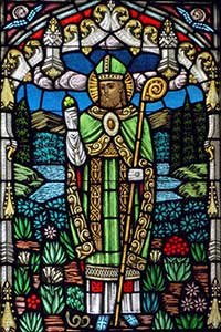 Stained glass window image of Saint Patrick wearing green, with shamrock and snake.
