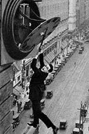 Man hanging from clock high above city street.